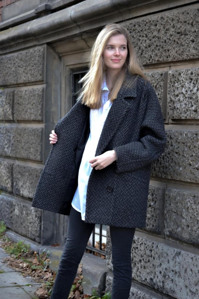 Frau präsentiert einem grauen schicken Mantel, der im Store gekauft werden kann.